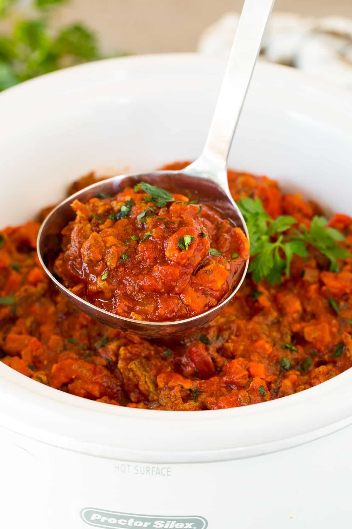 A ladle holding up a serving of slow cooker bolognese sauce.