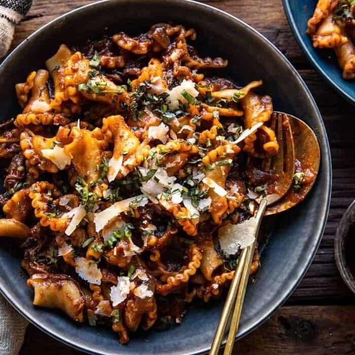 A picture of slow cooker red wine braised short rib pasta in a blue bowl with a fork and spoon.
