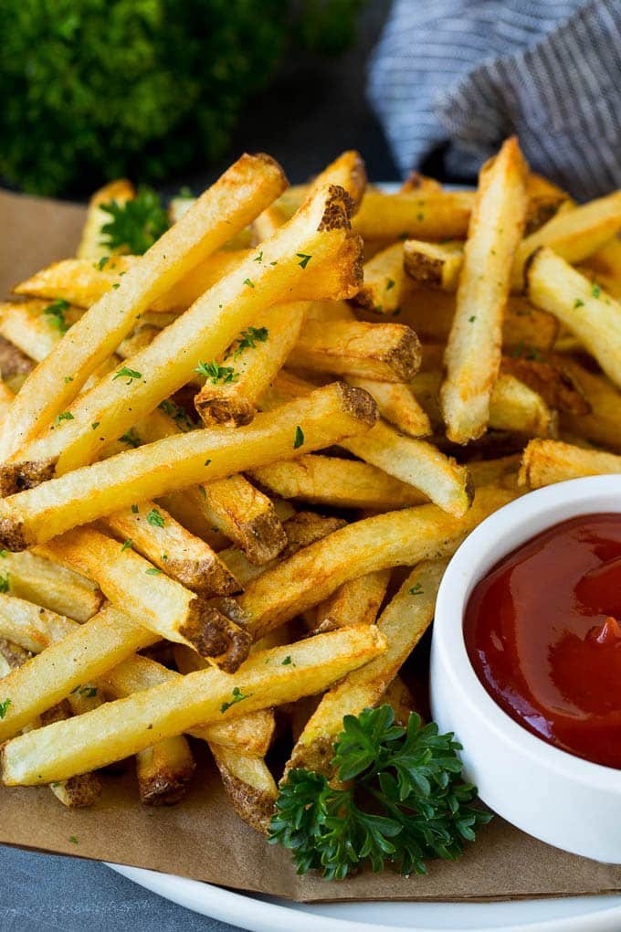 A plate of kitchen-made french fries served with a bowl of ketchup.