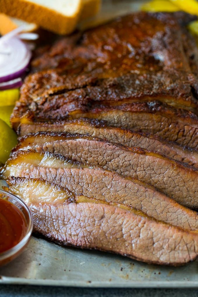 Sliced smoked brisket with a side of BBQ sauce.
