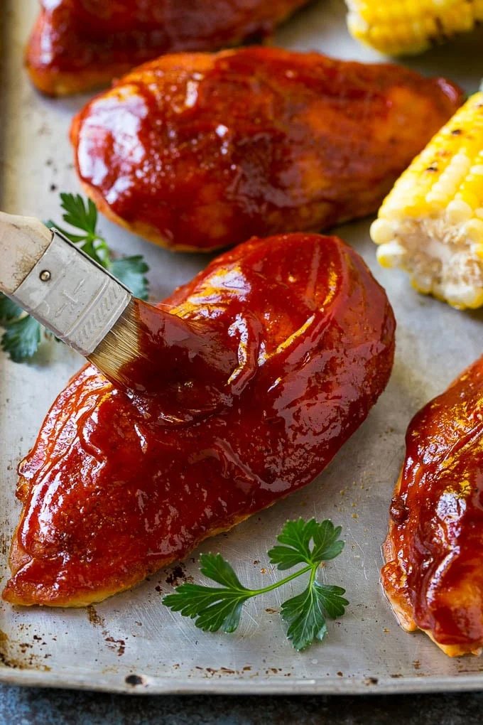 Smoked chicken breasts being brushed with BBQ sauce.