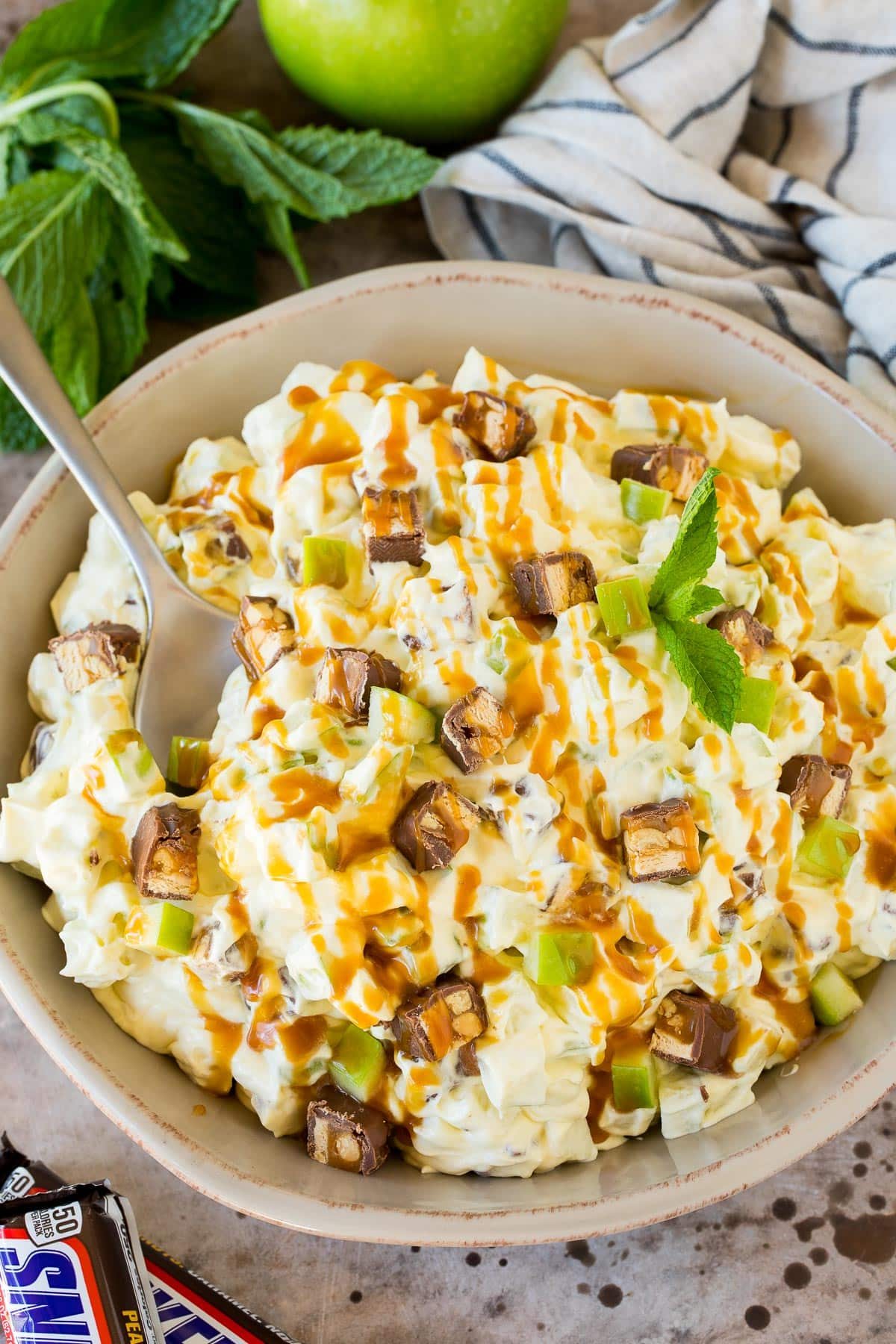 A bowl of snicker apple salad topped with caramel sauce.
