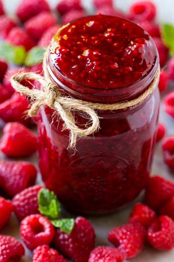 A jar of kitchen-made raspberry sauce surrounded by fresh raspberries.