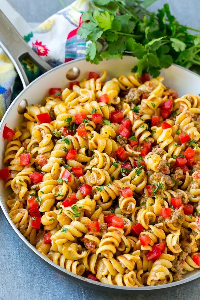 A skillet of taco pasta topped with fresh diced tomatoes and cilantro.