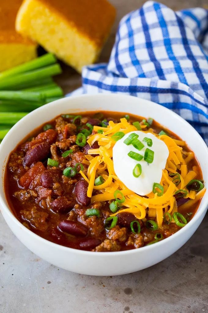 A bowl of beef chili topped with cheese, sour cream and green onions.