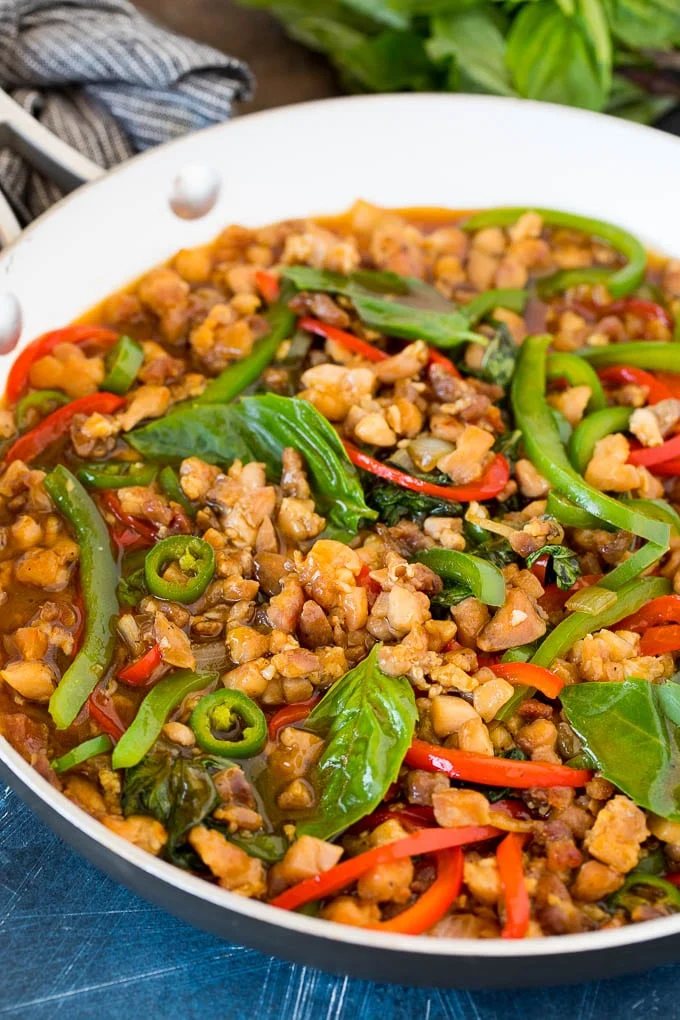 A pan of Thai basil chicken with peppers and fresh basil leaves.