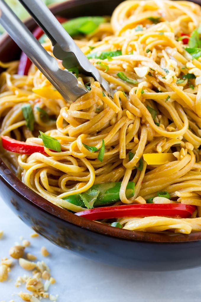 Tongs serving up a portion of Thai peanut noodles.