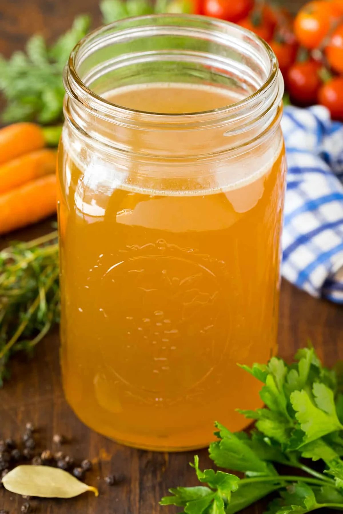 A jar of kitchen-made turkey broth surrounded by herbs and vegetables.