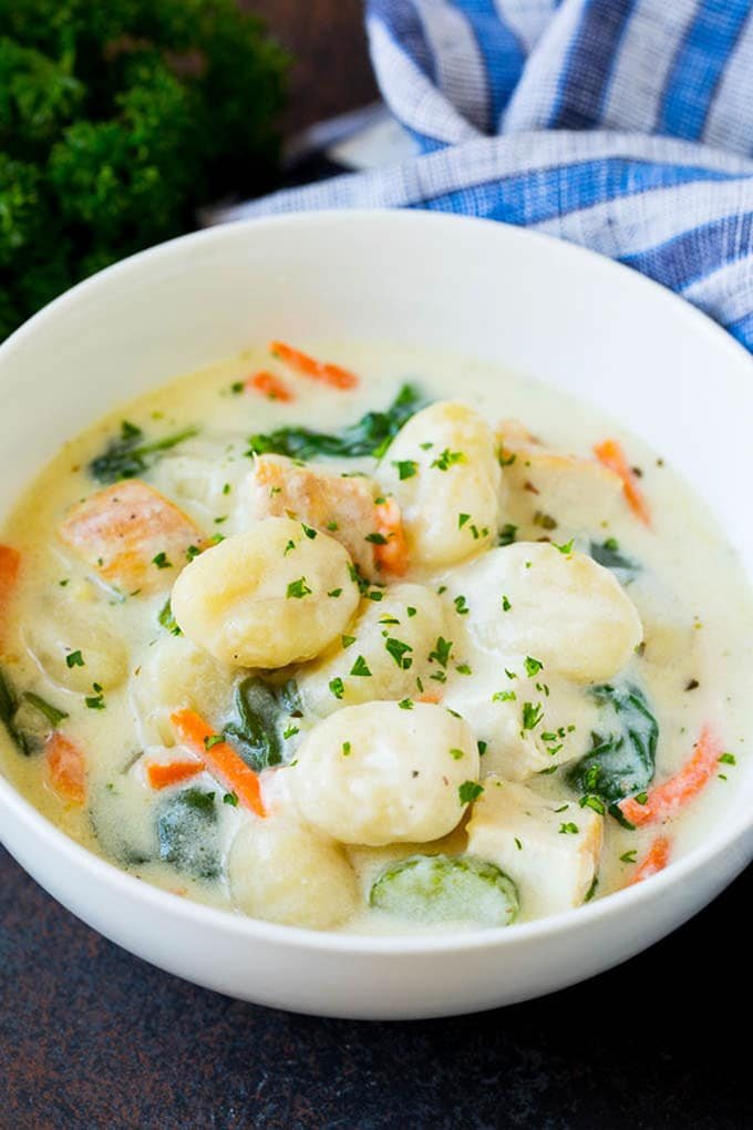 A bowl of silky gnocchi soup topped with chopped parsley.