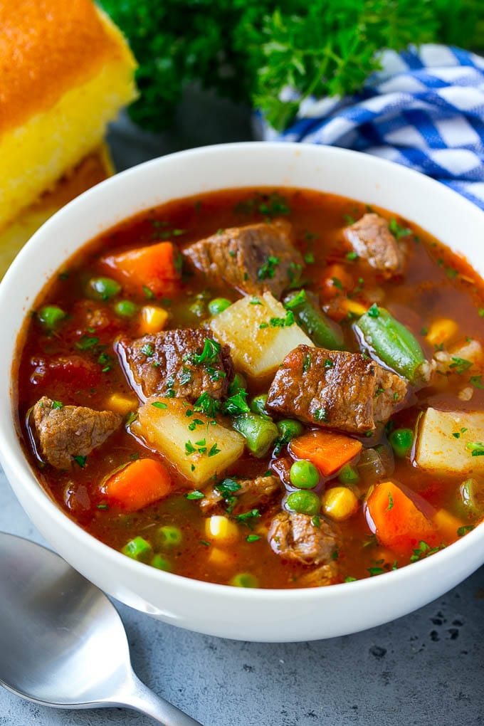 A bowl of vegetable beef soup with carrots, celery, onions, potatoes, tomatoes, corn and peas.