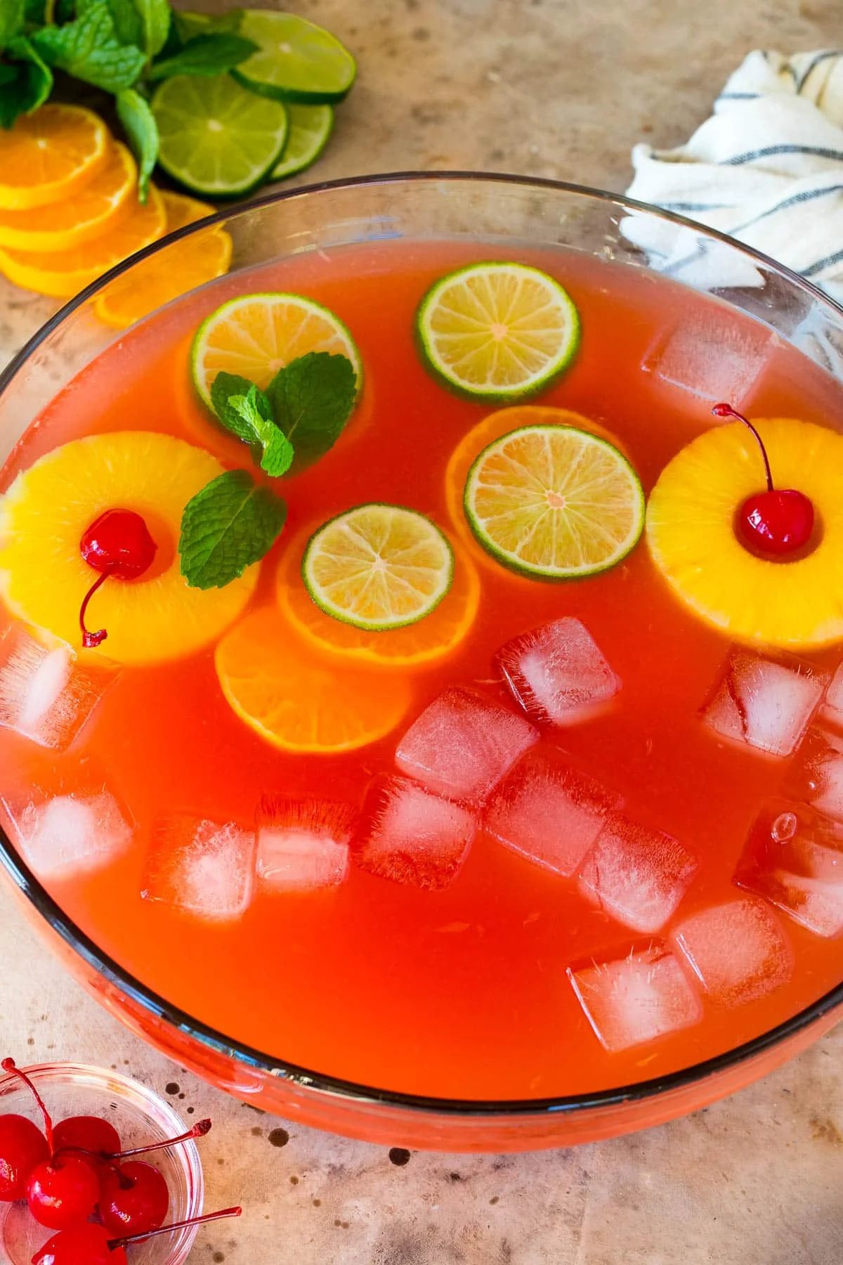 A bowl of vodka punch with citrus slices, pineapple and cherries in it.