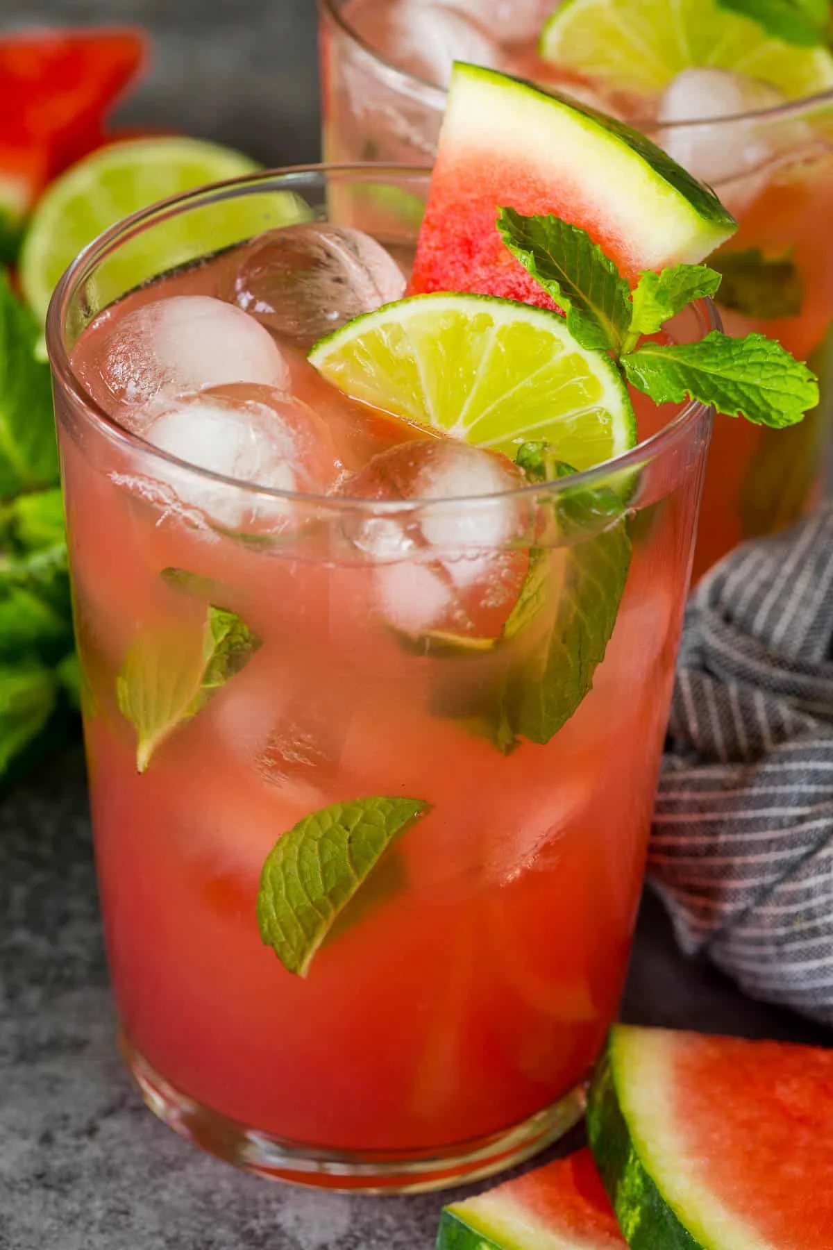 A glass of watermelon mojito with a slice of watermelon and lime wedge on top.