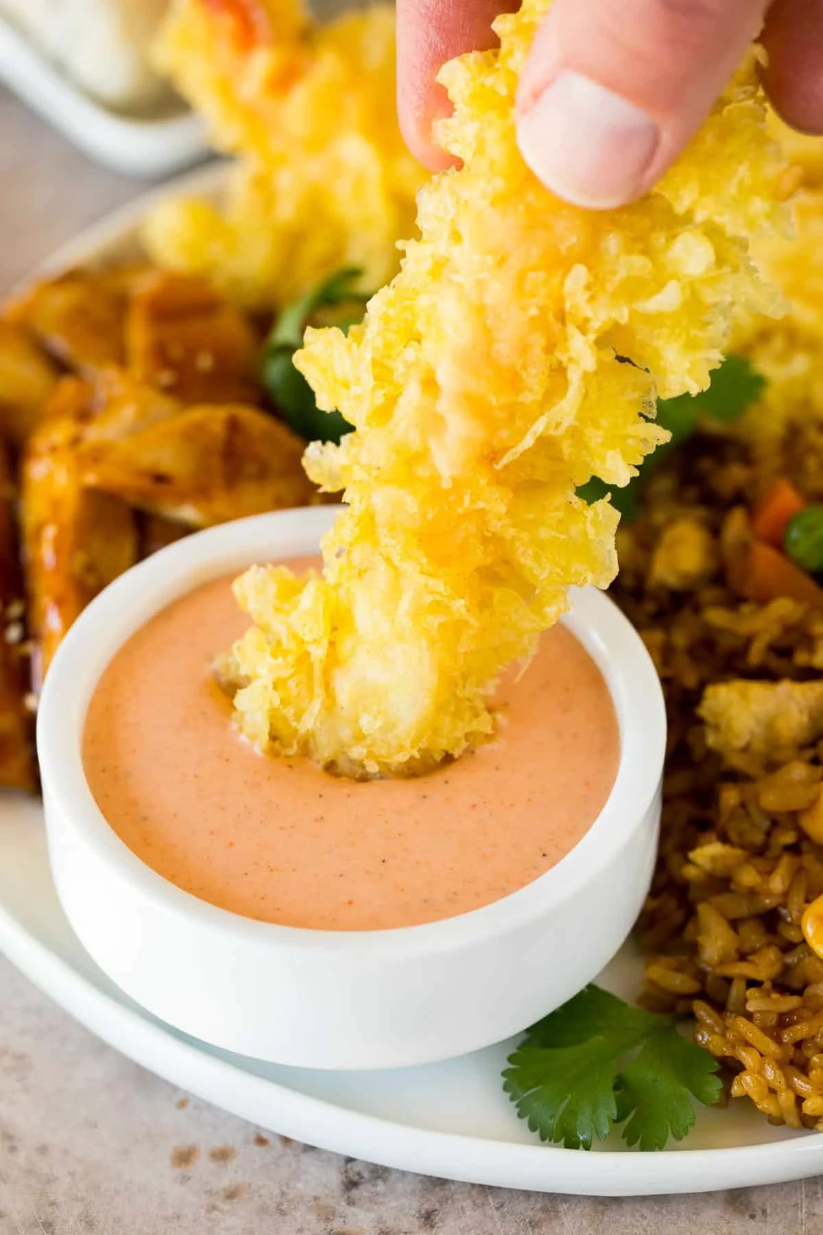 A hand dipping a tempura shrimp into yum yum sauce.