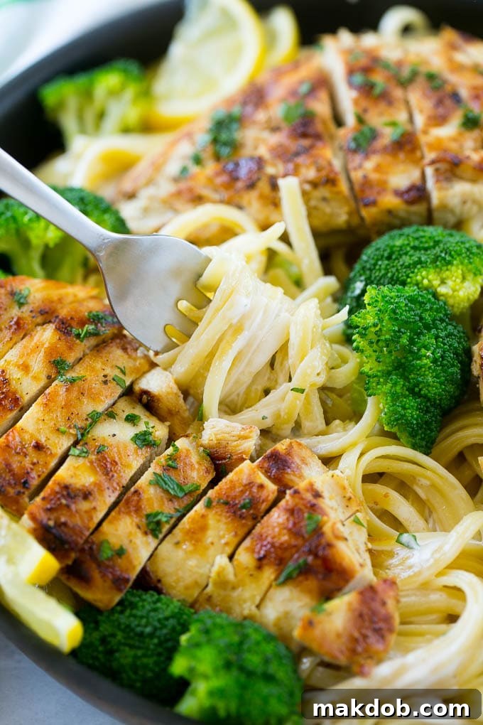 A forkful of creamy lemon pasta surrounded by chicken and broccoli.