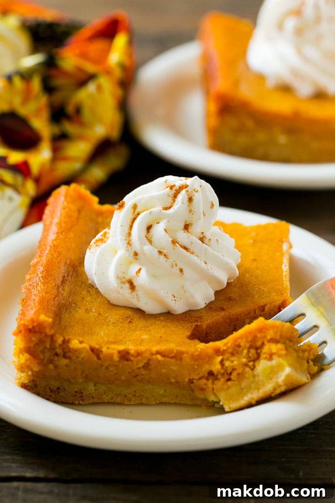 Decadent Pumpkin Gooey Squares 2 A golden-brown slice of Pumpkin Gooey Butter Cake, revealing its distinct chewy crust and creamy pumpkin layer, with a fork gently resting in it.