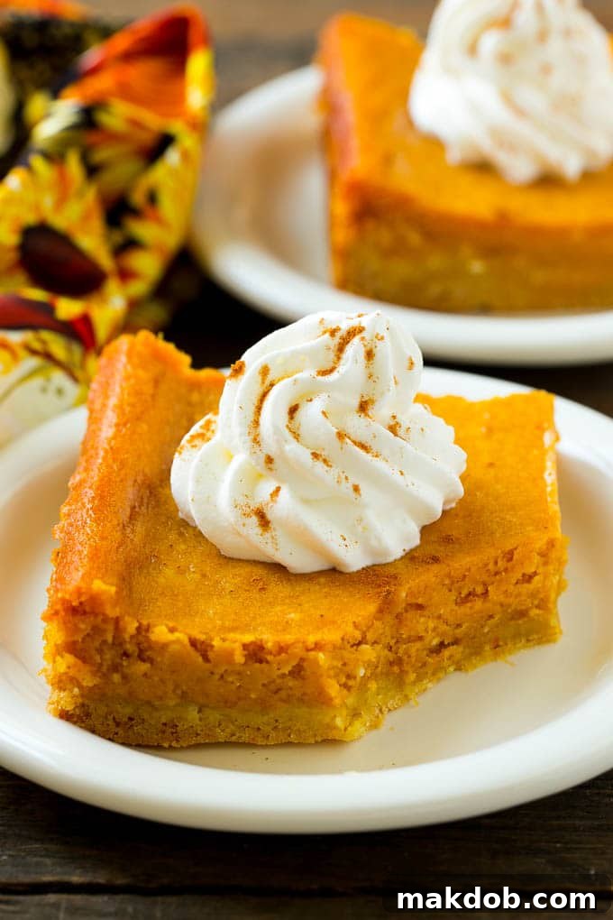 Pumpkin Gooey Butter Cake Recipe | Pumpkin Cake Recipe | Gooey Butter Cake | Pumpkin Dessert | Thanksgiving Dessert #pumpkin #cake #pumpkincake #gooeybuttercake #dessert #dinneratthezoo A close-up shot of a slice of pumpkin gooey butter cake, revealing the distinct layers of crust and filling, with a small bite taken out of it.