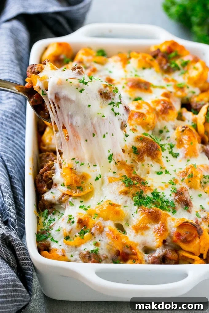 A pan of cheesy baked tortellini with a spoon lifting up a portion, showcasing the melted cheese and hearty sauce.