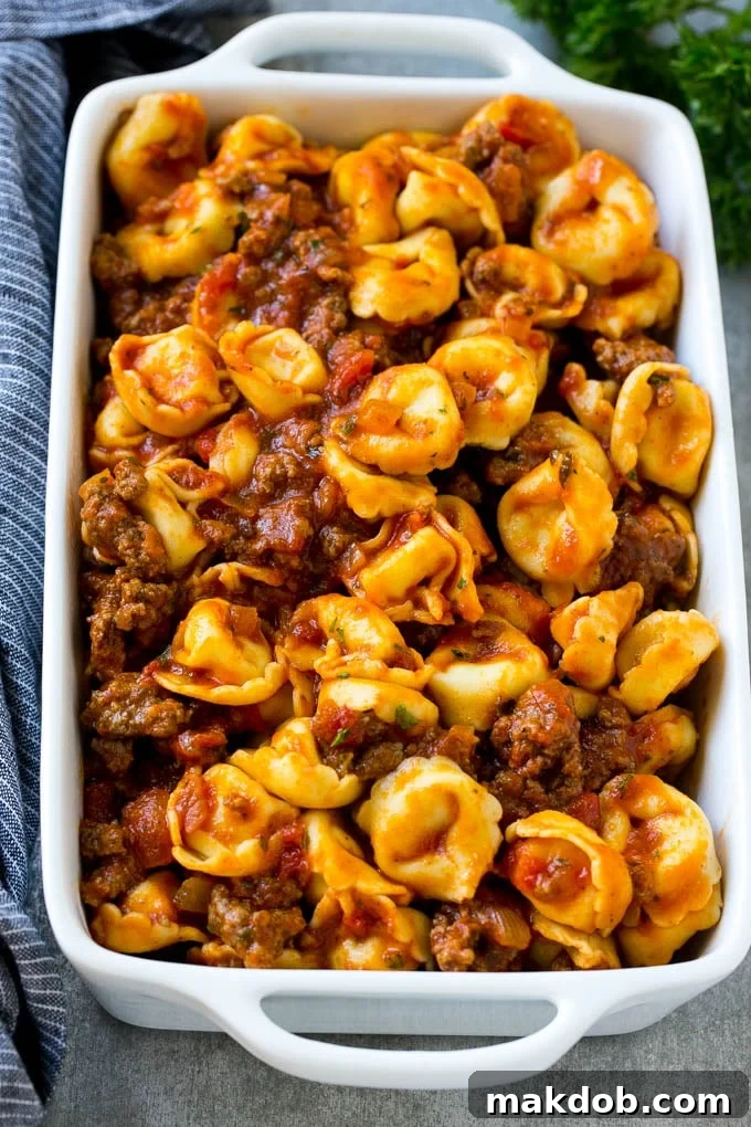 A dish of cheese tortellini generously tossed in a rich meat sauce, ready for baking.