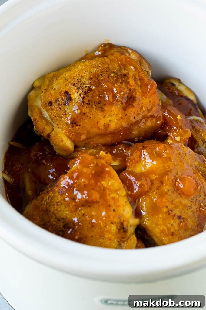 Chicken thighs and sliced onions in a slow cooker, covered with a rich apricot, soy, and ginger sauce, ready to cook into tender apricot chicken.