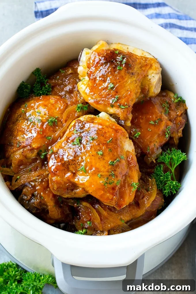 A slow cooker filled with perfectly cooked apricot chicken thighs, coated in a glistening sweet and savory sauce, garnished with fresh herbs.