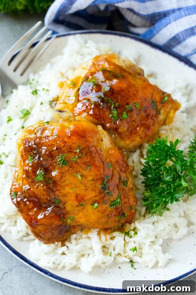 Two apricot chicken thighs on a plate over rice, garnished with parsley. A delicious and easy slow cooker meal.