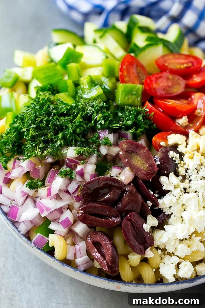 A bowl of pasta with red onion, kalamata olives, bell pepper and tomatoes, with a drizzle of Greek dressing.