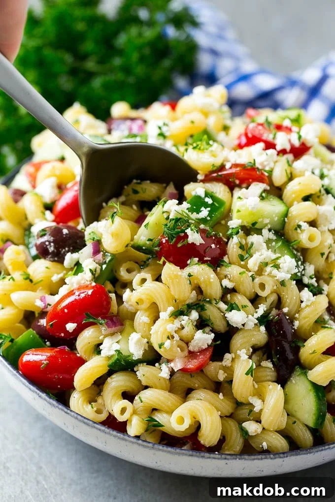 A bowl of Greek pasta salad with a serving spoon in it.