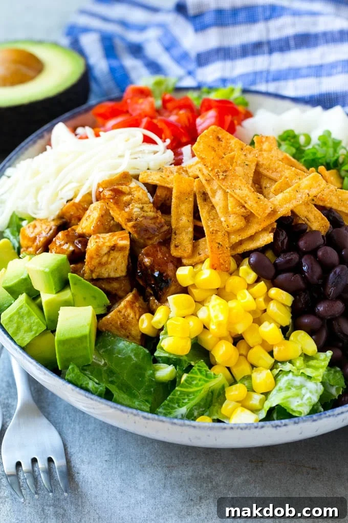 A close-up shot of the assembled BBQ chicken salad, showcasing layers of grilled chicken, fresh vegetables, beans, and crispy tortilla strips, ready to be enjoyed.