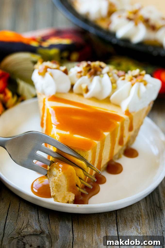 A fork cutting into a slice of creamy no bake pumpkin cheesecake with a graham cracker crust and a drizzle of caramel sauce.