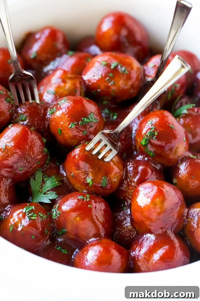 Cranberry Meatballs Recipe | Slow Cooker Meatballs | Slow Cooker Appetizer | Crockpot Meatballs A slow cooker filled with vibrant cranberry meatballs, garnished with fresh parsley, with cocktail forks nearby.
