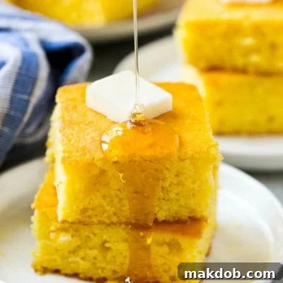 A stack of golden honey cornbread squares topped with melting butter and a drizzle of golden honey.