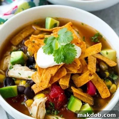 A bowl full of slow cooker chicken tortilla soup with avocado, sour cream and tortilla strips.