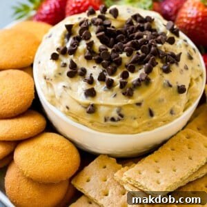 A bowl of delectable chocolate chip cookie dough dip, garnished with mini chocolate chips and served with graham crackers and vanilla wafers for dipping.