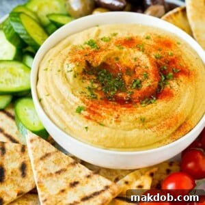 A serving bowl of homemade hummus, beautifully presented with warm pita bread and a selection of fresh vegetables for dipping.