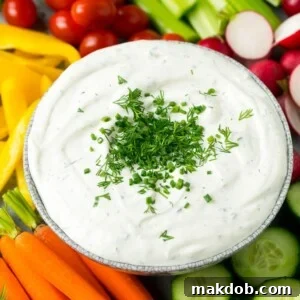 A creamy veggie dip generously topped with fresh herbs, served with an assortment of colorful, crisp vegetables for dipping.