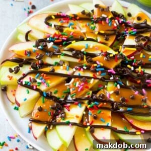 A plate of sliced apples topped with caramel and chocolate sauces, rainbow sprinkles and mini chocolate chips