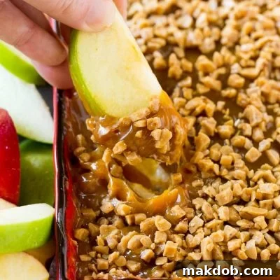 Decadent Caramel Apple Dip 2 A hand scooping out a serving of caramel apple dip, emphasizing its creamy texture.