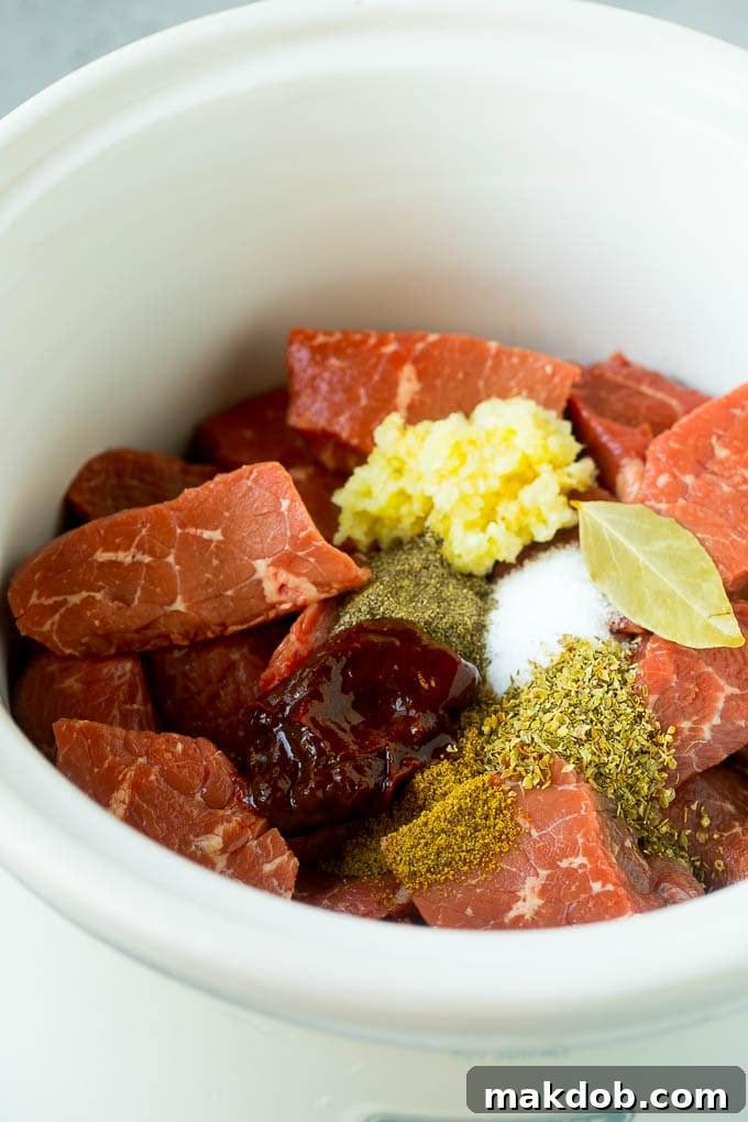 Slow Cooker Barbacoa | Beef Tacos | Crock Pot Beef Tacos #beef #tacos #crockpot #slowcooker #dinner #avocado #dinneratthezoo Cubes of beef, garlic, spices, and chiles in a slow cooker, ready for cooking.