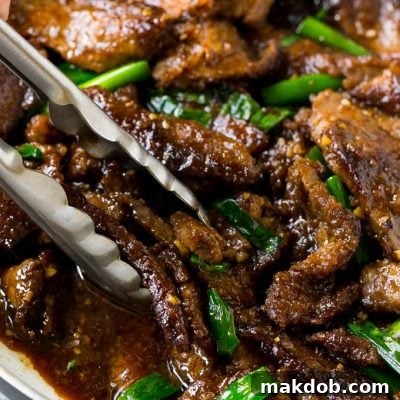A pan of Mongolian beef with tongs in it.