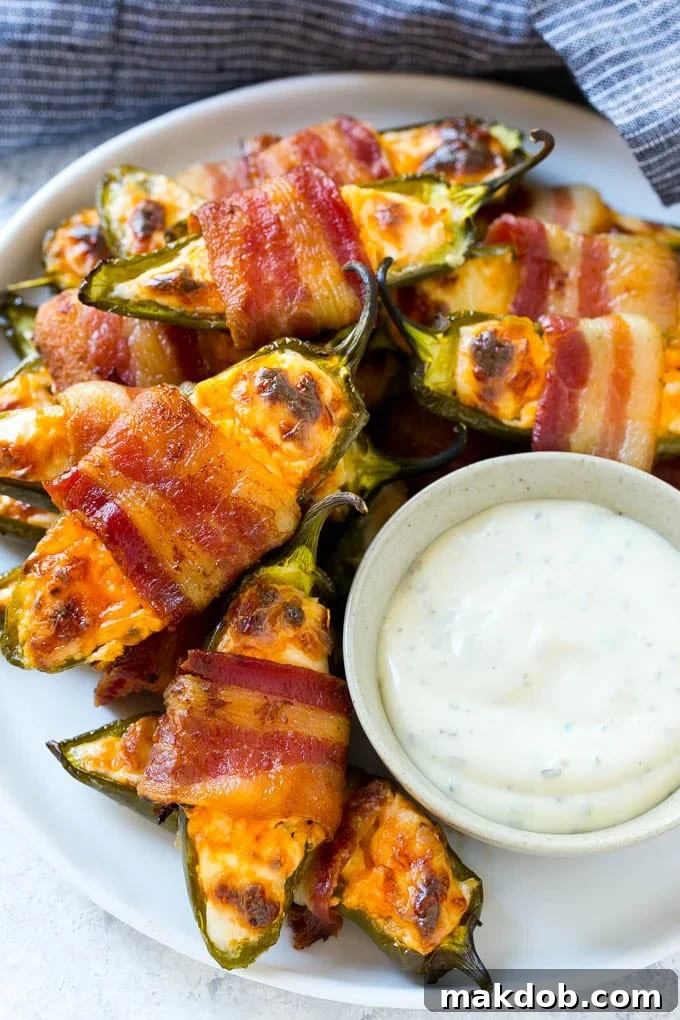 A plate full of bacon wrapped jalapeno poppers with a side of ranch for dipping.