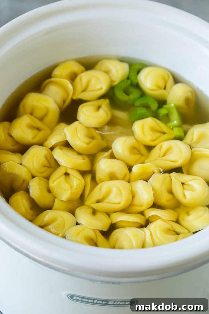 Fresh cheese tortellini submerged in hot chicken soup within a slow cooker.
