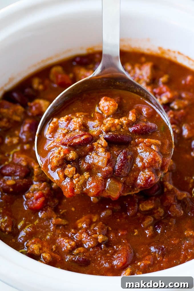 Hearty Slow Cooker Turkey Chili 6 A ladle serving up a generous portion of slow cooker turkey chili into a bowl.