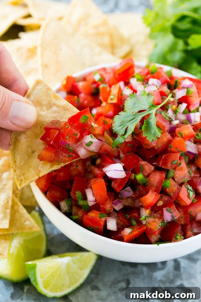 Vibrant Homemade Pico de Gallo 5 A hand reaching with a tortilla chip to scoop a generous portion of pico de gallo from a vibrant bowl.