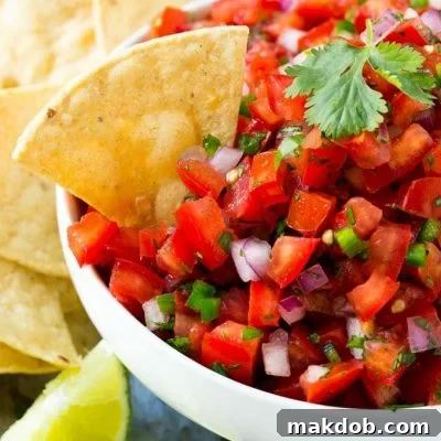 A bowl of pico de gallo with a tortilla chip in it, showcasing the fresh salsa.