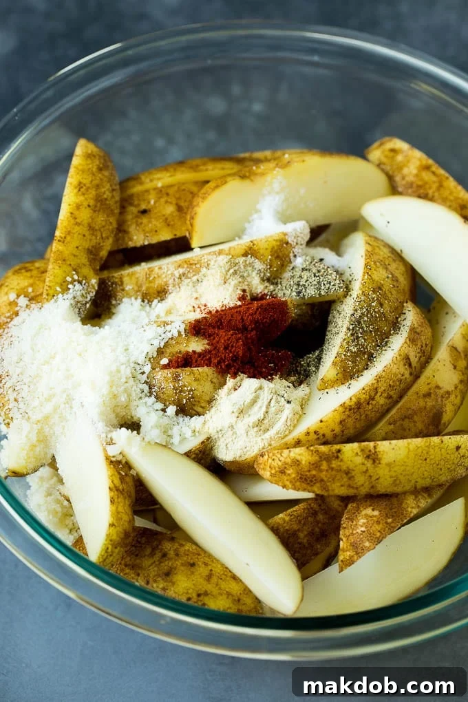 Sliced potatoes in a bowl with a variety of seasonings.