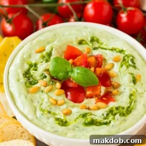 A bowl of pesto dipped topped with tomatoes and served with breads and vegetables.