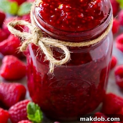 A jar of homemade raspberry sauce surrounded by fresh raspberries.