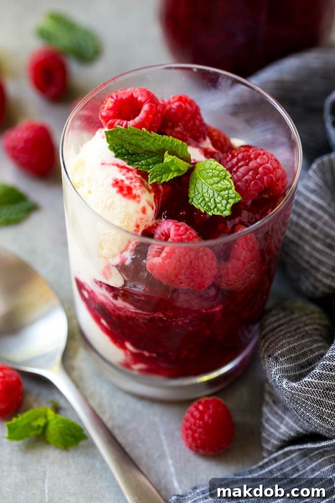 A cup of vanilla ice cream beautifully topped with homemade raspberry sauce and garnished with fresh raspberries.