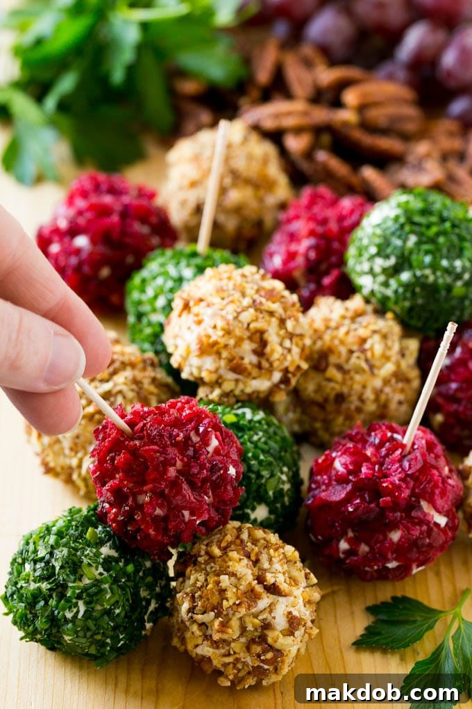 A hand elegantly reaching for an appetizer, a cheese ball bite generously crusted in vibrant dried cranberries, from a platter.