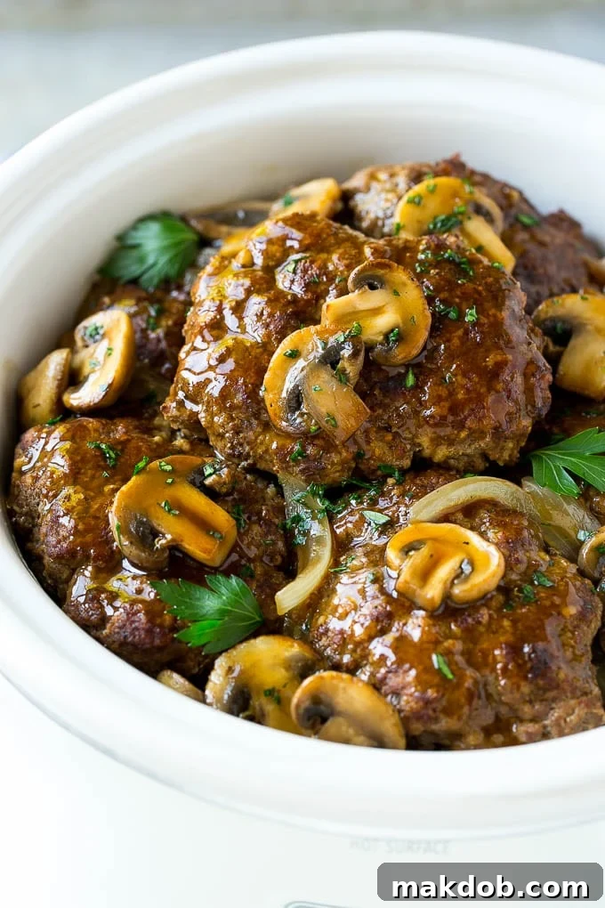 Slow Cooker Salisbury Steak Recipe | Homemade Salisbury Steak | Salisbury Steak from Scratch #steak #beef #salisbury #salisburysteak #slowcooker #crockpot #dinner #dinneratthezoo A crock pot with hamburger patties, cooked mushrooms and gravy.